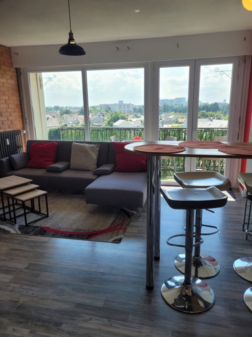Séjour moderne avec vue sur la ville, canapé sombre, coin bar et grandes fenêtres donnant sur Les Ponts de Cé
