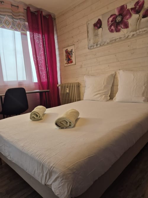 Chambre cosy de l'appartement Val'Déco avec lit blanc, serviettes roulées, rideaux bordeaux et art mural fleuri