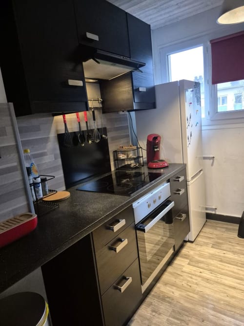 Cuisine moderne avec armoires noires, plans de travail foncés et électroménagers en acier inoxydable à l'appartement Val'Déco aux Ponts de Cé