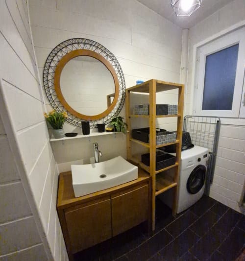 Salle de bains moderne avec lavabo rectangulaire blanc, meuble en bois, miroir rond décoratif et lave-linge à Val'Déco