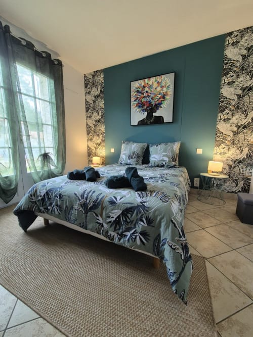 Chambre moderne avec mur d'accent bleu-vert, literie aux motifs tropicaux et œuvres d'art colorées à l'appartement Val'Déco Conciergerie