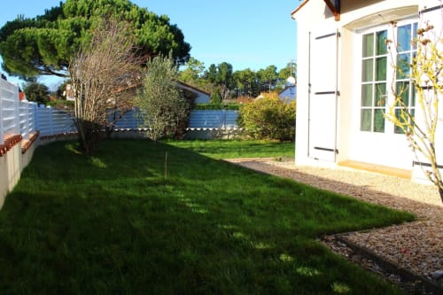 Spacieux jardin avec appartement à Val'Déco Conciergerie : pelouse impeccable, cottage blanc, arbres ombragés et clôture bleue