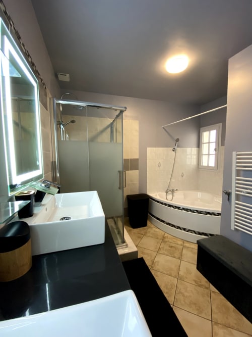 Salle de bain moderne à Val'Déco Conciergerie avec vasques blanches, baignoire courbe, douche vitrée et sèche-serviettes électrique