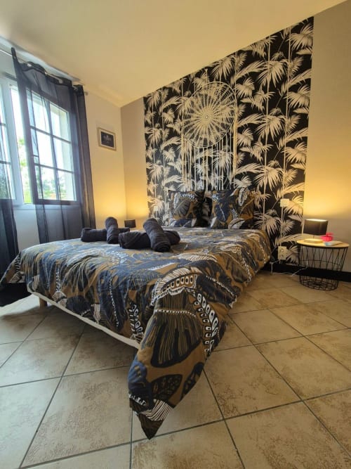 Chambre moderne à Val'Déco avec papier peint géométrique noir et or, literie décorée et vue sur le jardin