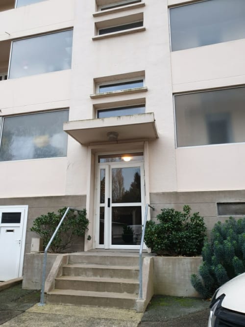 Entrée d'immeuble moderne aux Ponts de Cé, façade blanche, escaliers en béton, rampe métallique et aménagement paysager verdoyant