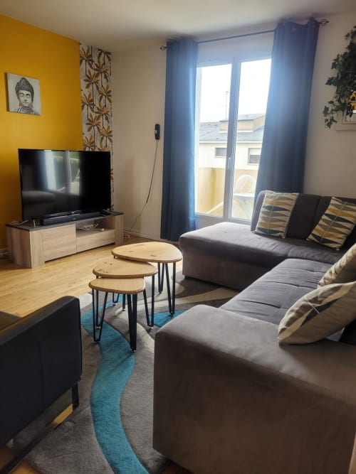Salon moderne avec canapé gris, TV, mur jaune et vue sur la ville - Val'Déco Conciergerie, Les Ponts de Cé