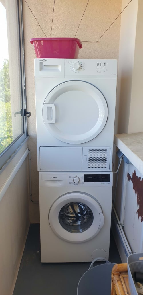 Appareils de blanchisserie empilés dans l'appartement Val'Déco, Les Ponts de Cé. Machine à laver en bas, sèche-linge en haut avec du linge rose