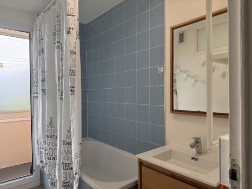 Salle de bain moderne de l'appartement Val'Déco à Les Ponts de Cé avec carrelage bleu, lavabo, douche et fenêtre vue sur la ville