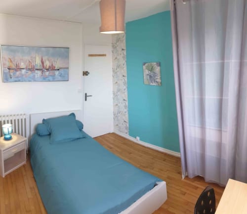 Chambre moderne à Val'Déco Conciergerie avec mur d'accent turquoise, lit simple, parquet et vue sur la ville aux Ponts de