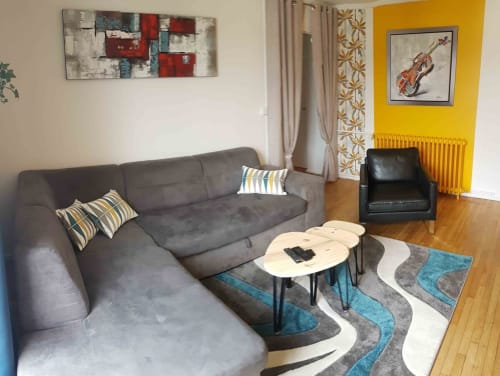 Séjour moderne de l'appartement Val'Déco aux Ponts-de-Cé avec canapé gris, tapis géométrique et mur jaune