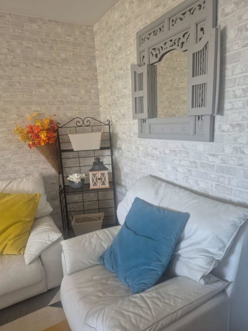 Appartement cozy Val'Déco aux Ponts de Cé : murs en briques blanches, coussins bleus sur canapé crème et étagère décorée