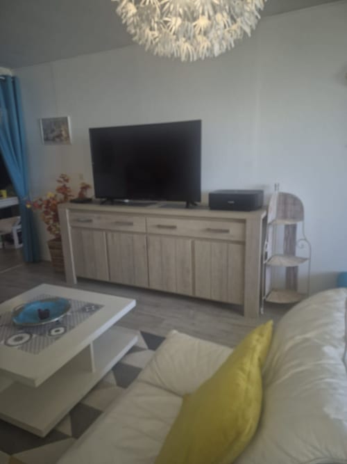 Salon moderne de la conciergerie Val'Déco avec télévision, mobilier en bois clair et touches jaunes
