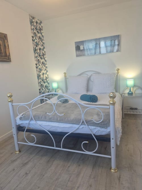 Chambre moderne avec lit en métal blanc orné, lampes turquoise et art géométrique à Val'Déco Conciergerie, Les Ponts