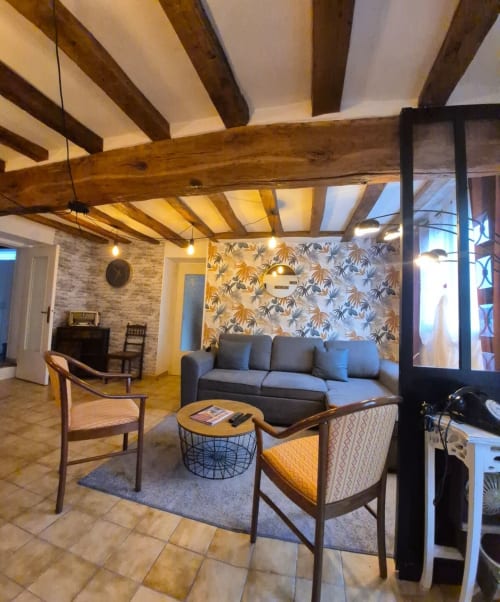 Le lounge de la conciergerie Val'Déco aux Ponts de Cé : poutres en bois, canapé gris, fauteuils rétro et papier peint motifs.