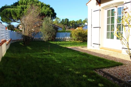 Jardin ensoleillé de Val'Déco Conciergerie aux Ponts de Cé avec pelouse verte, maison blanche et arbres méditerranéens