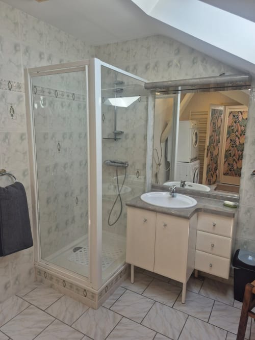 Salle de bain moderne avec douche en verre, lavabo blanc et murs en carrelage motifs chez Val'Déco Conciergerie