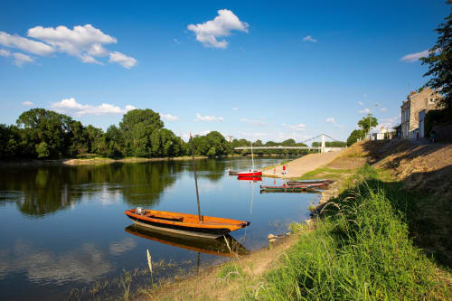 Bateaux colorés amarrés sur la Sarthe aux Ponts de Cé, France, avec une végétation luxuriante et une architecture historique