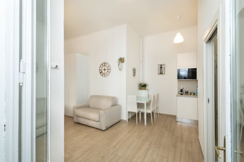 Modernes Wohnzimmer im Magnolia Apartments Milan mit beigem Sofa, Esstisch, Küchenzeile, Holzböden und weißer Einrichtung