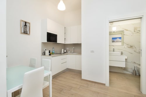 Moderne Küche und Essbereich in den Magnolia Apartments Mailand mit weißen Schränken, sichtbares Marmorbadezimmer durch die offene Tür