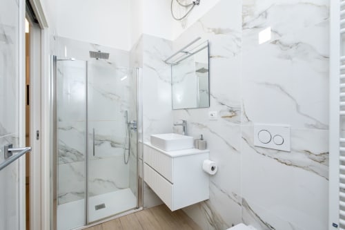 Modernes Badezimmer in den Magnolia Apartments Mailand mit Marmor Wänden, Glasdusche, weißem Waschbecken und verchromten Armaturen