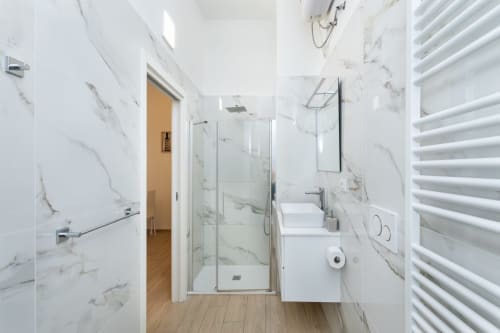 Modernes Badezimmer in den Magnolia Apartments Milan mit Marmormauern, Glasdusche, weißem Waschtisch und beheiztem Handtuchhalter