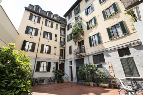 Innenhof der Magnolia Apartments Mailand mit cremefarbenem Wohngebäude, grüner Bepflanzung und Ziegelpflaster