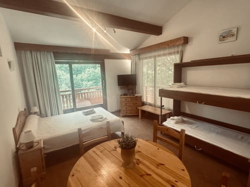 Chambre lumineuse aux Studios Hôtel La Rochetaillée à Brides-les-Bains avec poutres en bois, lits superposés et vue sur les montagnes