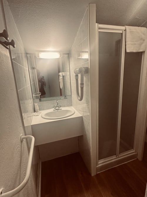 Salle de bains moderne à l'Hôtel Studios La Rochetaillée à Brides-les-Bains avec lavabo blanc, miroir, cabine de douche et bois