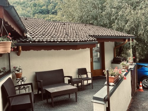 Espace de détente extérieur à l'Hôtel Studios La Rochetaillée à Brides-les-Bains avec mobilier sombre, fleurs en pots et cadre forestier