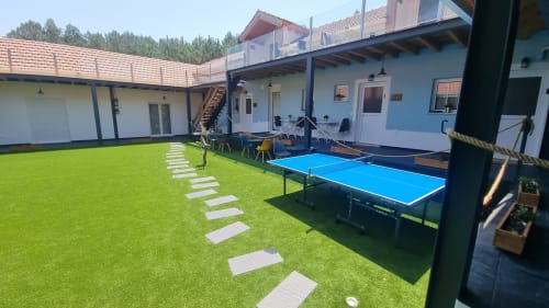 Pátio do Charm Discovery Experiences em Leiria com gramado verde, pedras de passagem, mesa de ping-pong azul e design branco moderno