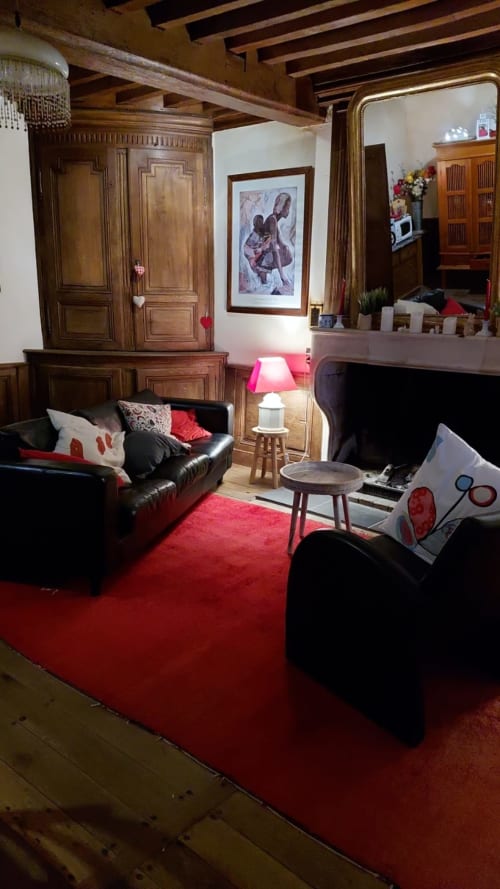Salon cosy de la Maison de Marie-Claire B&B avec tapis rouge, canapé en cuir noir et poutres apparentes