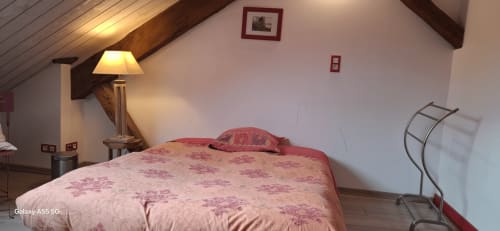 Chambre douillette à La Maison de Marie-Claire avec literie rose fleurie, lampe et vue sur le jardin.
