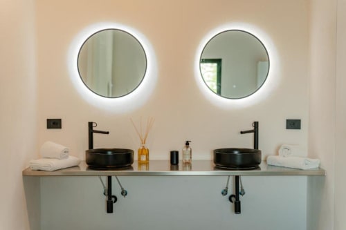 Bagno moderno presso Tenuta Alela con doppi lavabi neri, specchi illuminati, asciugamani bianchi e arredamento minimalista