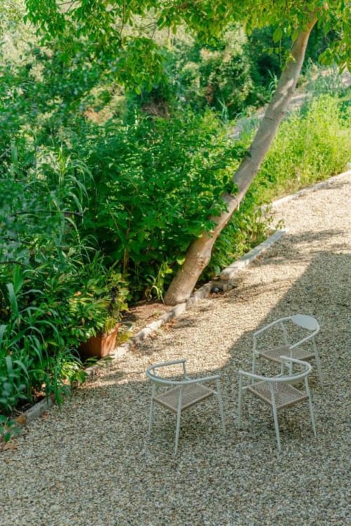 Patio in ghiaia ombreggiato con sedie metalliche presso Tenuta Alela, circondato da lussureggiante vegetazione e alberi maestosi a Figline