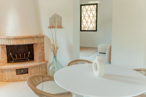 Sala da pranzo nella dependance di Tenuta Alela con tavolo rotondo, sedie in vimini, camino e vista sul giardino a Figline Valdarno