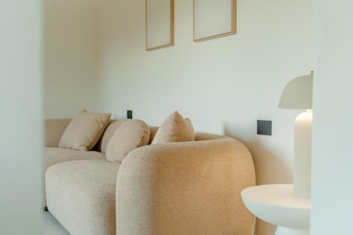 Soggiorno minimalista moderno presso Tenuta Alela con divano curvo color crema, cornici in legno e illuminazione soft in una barn suite