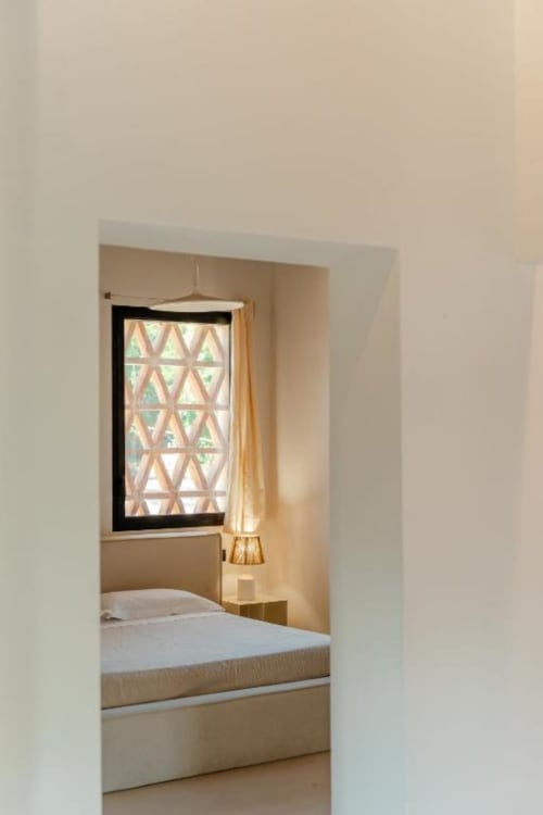 Camera da letto accogliente a Tenuta Alela con biancheria bianca, lampada a sospensione e finestra con motivi geometrici con vista sul giardino