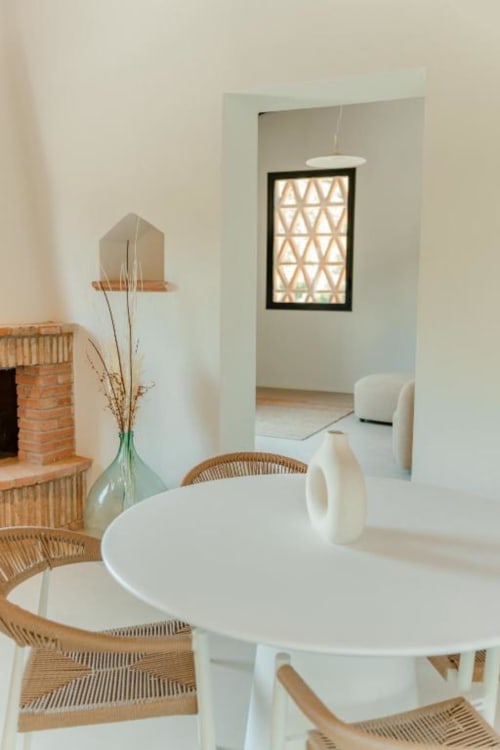 Moderna sala da pranzo della dependance Tenuta Alela con tavolo rotondo bianco, sedie intrecciate e vista sul giardino attraverso l'arcata