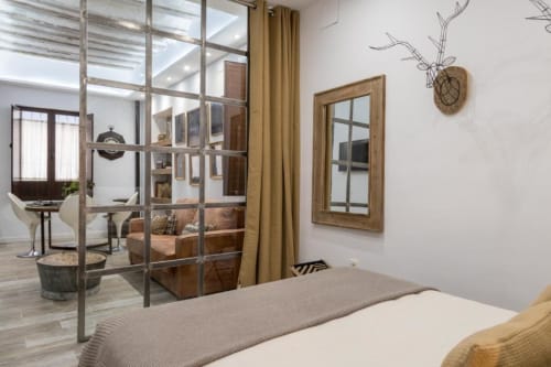 Moderno dormitorio loft en CTH Granada con mamparas de cristal, sofá marrón, pared espejada y detalles de madera