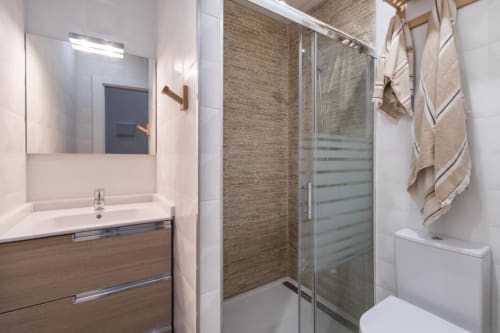 Baño moderno en el apartamento CTH Granada Loft Gracia con vanidad de madera, espejo, ducha con mampara de vidrio y inodoro blanco