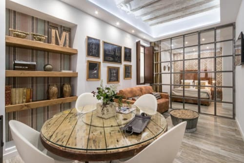 Suite moderna del hotel CTH Granada con mesa redonda de madera, sillas blancas, estanterías de madera y divisiones de cristal