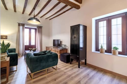 Salón moderno en Green Apartment de CTH Granada con sofá verde, vigas de madera, muebles oscuros y vistas a la ciudad