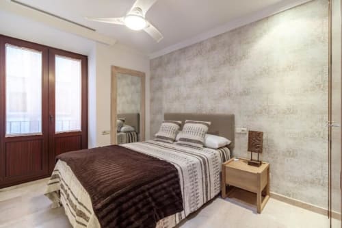 Dormitorio moderno en apartamento CTH Granada, Armilla con cama de matrimonio, puertas al balcón, papel tapiz texturizado beige y mesita de noche de madera