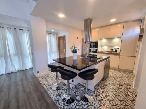 Cocina y comedor modernos en Penthouse Gracia de CTH Granada con isla de encimera negra, barra de asientos y mueblería crema
