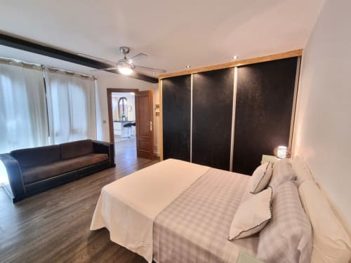 Amplio dormitorio principal en Penthouse Gracia de CTH Granada con cama queen, armario negro, sofá de cuero y vistas a la ciudad