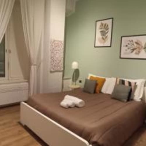 Camera luminosa presso AD Trastevere Guest House Roma con pareti verde salvia, letto marrone, cuscini, arte botanica e tende bianche