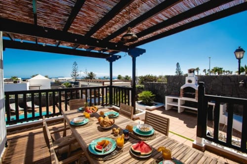 Terraza de Villa Cavendish con mesa de comedor, vistas al mar, pérgola y horno de pizza blanco en Playa Blanca