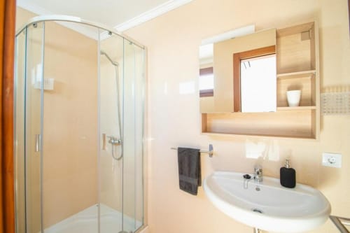 Baño moderno en Villa Cavendish, Playa Blanca, con ducha de cristal, lavamanos blanco, espejo de botiquín y azulejos en tonos beige cálido
