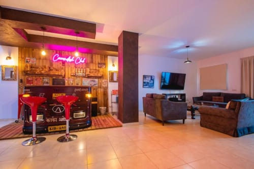 Salón de entretenimiento retro en Villa Cavendish con letrero de neón, exhibición de autos vintage, asientos marrones y TV de pantalla plana