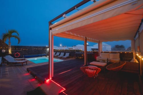 Terraza de Villa Cavendish al atardecer con pérgola roja iluminada, piscina, tumbonas y vistas al mar en Playa Blanca